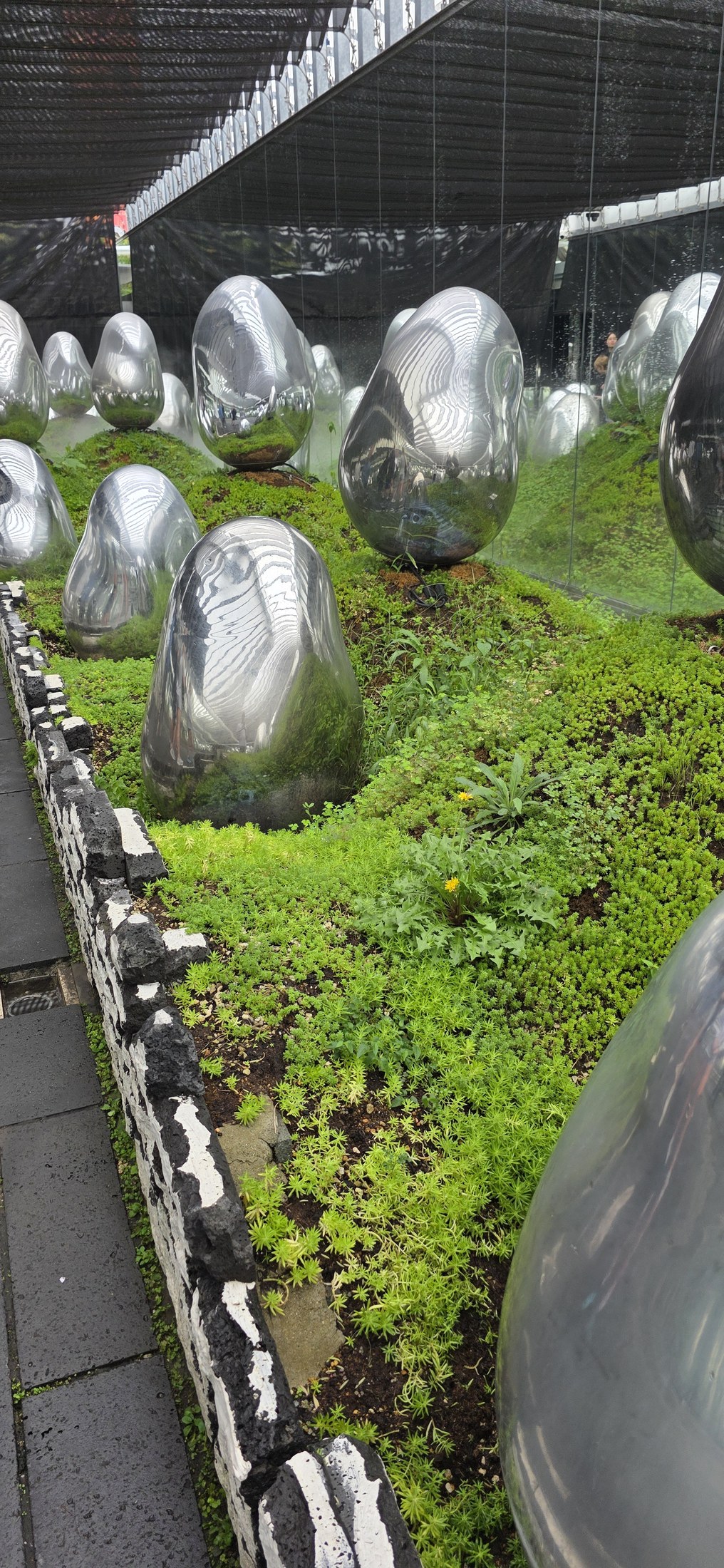 Kunstinstallation mit reflektierenden Skulpturen und grüner Bepflanzung